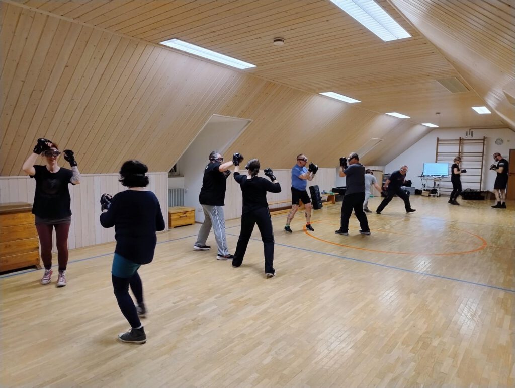 Gemischte Trainingsgruppe übt paarweise mit erhobenen Händen und Schutzbrillen