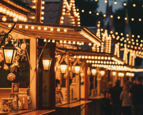Festlich beleuchtete Volksfest-Buden am Abend mit Lichterketten und Menschen im Hintergrund